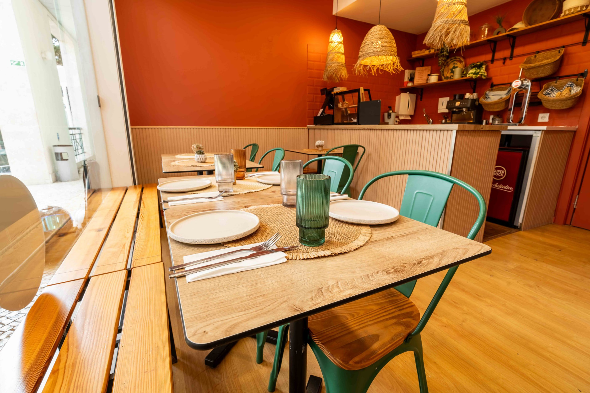 Mesa posta com pratos de cerâmica, copos canelados e individuais de fibra natural junto ao balcão.